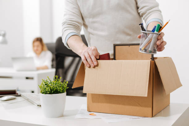 Taking a gap. Concentrated involved melancholy employee standing and packing the box with his belongings while leaving the company and expressing sadness